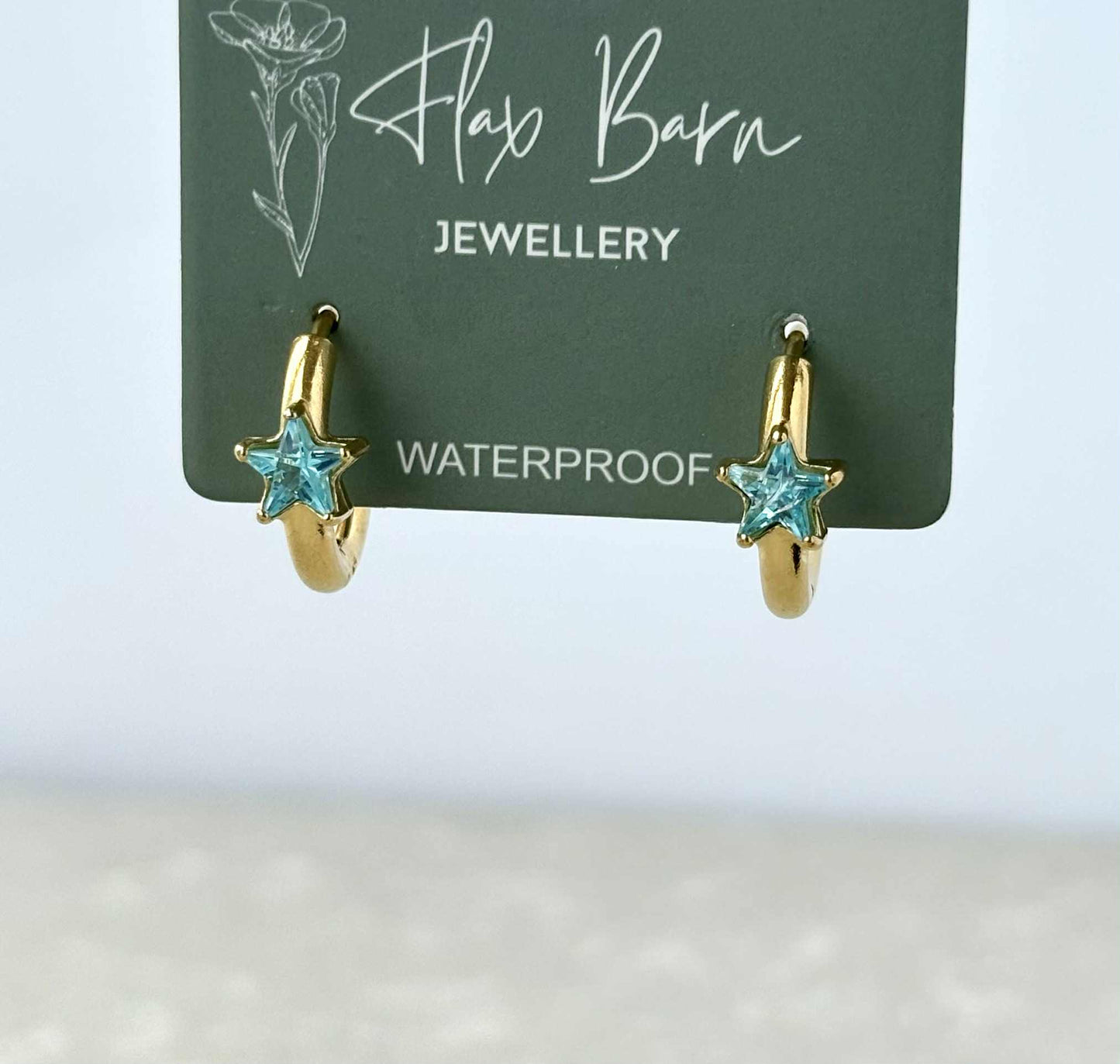 Gold hoop earrings with turquoise star stones on a Flax Barn Jewellery card.